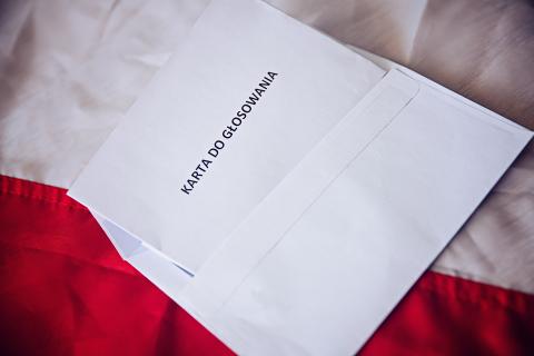 Koperta z wysuniętą kartką z napisem "Karta do głosowania" leży na biało-czerwonej fladze