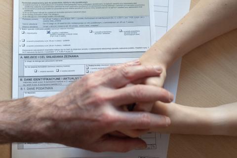 męska dłoń obejmuje złączone dłonie kobiety na formularzu podatkowym 