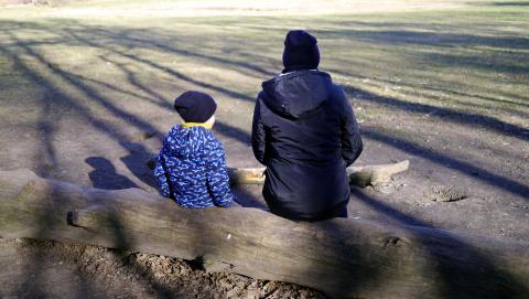 Kobieta i kilkuletnie dziecko siedzą tyłem do kadru na obalonym pniu 