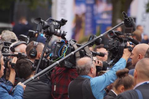dziennikarze z kamerami prowadzą wywiad z zasłoniętą przez nich osobą 