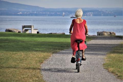 widziana z tyłu seniorka jedzie rowerem nad jeziorem 