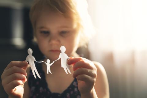 Smutna dziewczynka trzyma w dłoniach wycinankę w kształcie sylwetek ojca, matki i dziecka