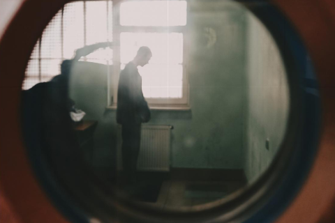 stojący mężczyzna w celi więzienia widziany przez wizjer w drzwiach