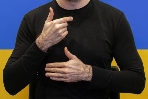 osoba posługująca się językiem migowym na tle flagi Ukrainy