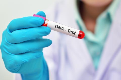 Lekarz trzymający fiolkę z czerwonym płynem i naklejką "DNA Test"