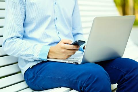 siedzący mężczyzna z laptopem na kolanach i smartfonem w dłoni