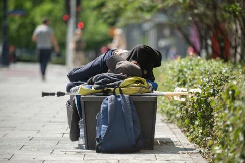 osoba śpi na ławce ma której leżą też kule i różne rzeczy