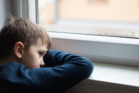 Smutne dziecko wygląda przez okno opierają się na parapecie