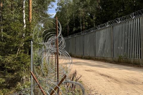 Wysoki płot z drutem kolczastym stojący wzdłuż leśnej drogi