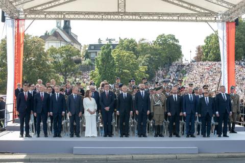 Duża grupa osób, wśród nich RPO Marcin Wiącek, stoi na trybunie, po bokach której wywieszone są flagi Polski