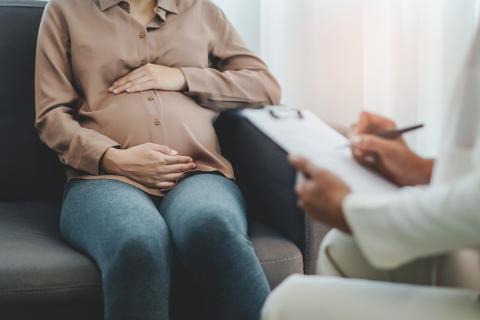 siedząca kobieta w ciąży trzyma się za brzuch  obok siedzi lekarz 