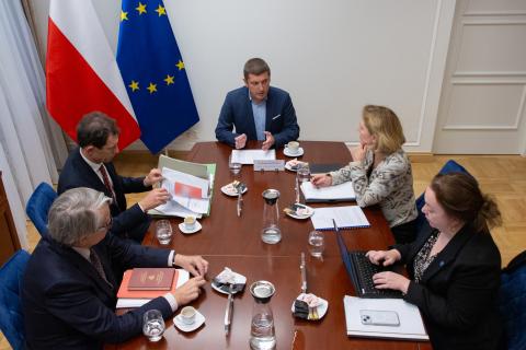 ZRPO Wojciech Brzozowski rozmawia z gośćmi przy konferencyjnym stole. W tle flagi Polski i Unii Europejskiej