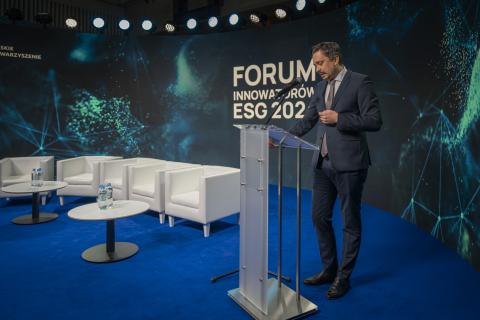 Osoba stoi na scenie za mównica i przemawia na tle dużego napisu "Forum Innowatorów ESG 2024"