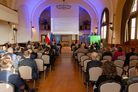 Kilkadziesiąt osób siedzi na sali i słucha wystąpienia, w tle na wyświetlaczu biały napis na granatowym tle "Konferencja z okazji 20-lecia Pełnomocnika Terenowego RPO we Wrocławiu"