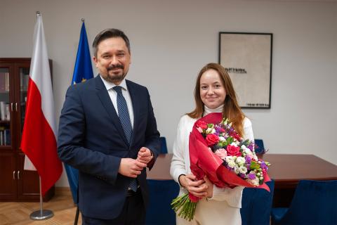 RPO Marcin Wiącek i trzymająca bukiet kwiatów Jolanta Ożga uśmiechają się pozując do zdjęcia w gabinecie RPO