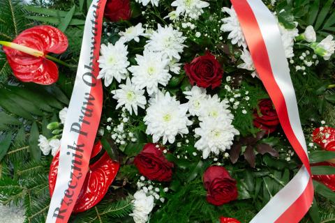 Zielony wieniec z białymi i czerwonymi kwiatami i biało-czerwoną wstążką z napisem Rzecznik Praw Obywatelskich