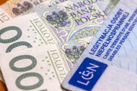 Legitymacja osoby z niepełnosprawnością leżąca na banknotach 100 i 200-złotowych