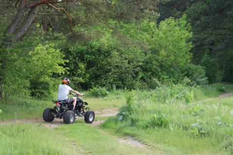 Osoba siedząca na qudzie na leśnej drodze