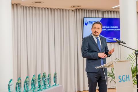 Marcin Wiącek stoi przy podium i wypowiada się do mikrofonu