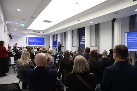 Marcin Wiącek wypowiada się stojąc przy mównicy. Wokół niego na widowni siedzi kilkadziesiąt osób