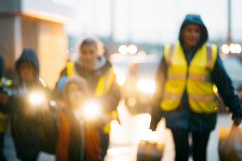 trzy osoby w jaskrawych kamizelkach idą w deszczu z torbami 