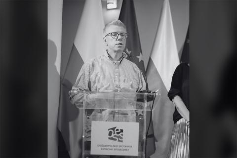 Czarno-biały portret Cezarego Miżejewskiego przemawiającego przy podium