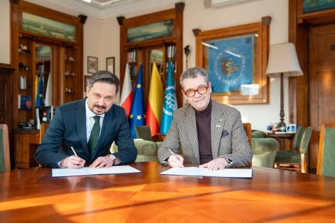 Dwie osoby siedzą za stołem i podpisują dokument