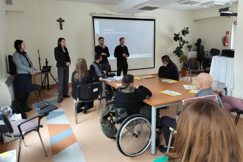 Kilkanaście osób siedzących przy stołach na sali konferencyjnej słucha wystąpienia