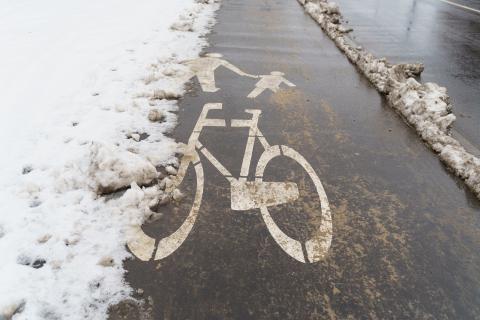 częściowo zaśnieżona droga z symbolem roweru i osoby trzymającej dziecko za rękę