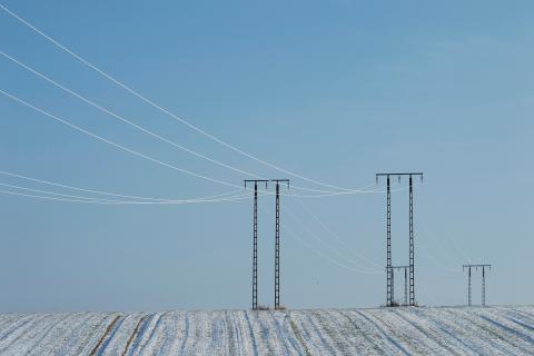 Słupy z liniami energetycznymi stojące na oszronionym polu