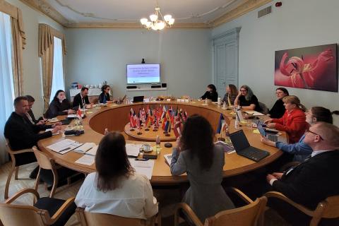 Kilkanaście osób dyskutuje siedząc wokół okrągłego stołu konferencyjnego