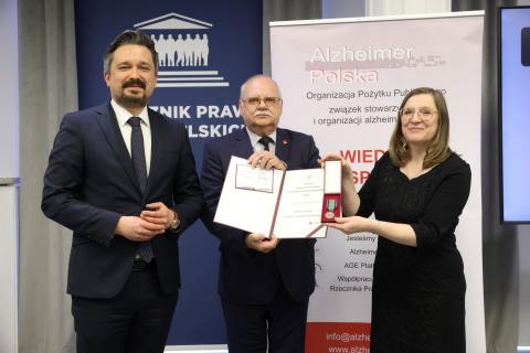 Trzy osoby pozują do wspólnego zdjęcia trzymając dyplom oraz odznakę w formie medalu