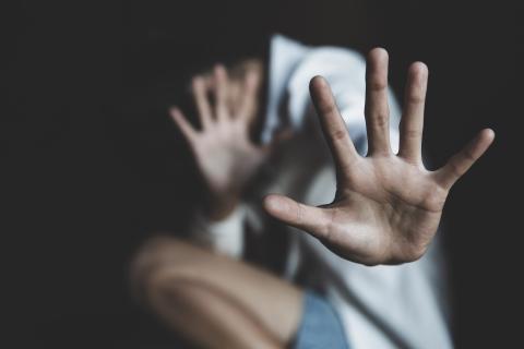 przykucnięta osoba na ciemnym tle odwraca się z rozcapierzonymi dłońmi