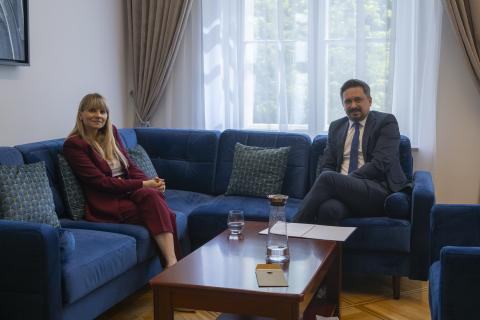 Dwie osoby siedzą na fotelach przy stoliku i pozują do wspólnego zdjęcia