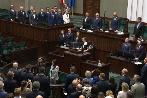 Osoba za mównicą sejmową odczytuje treść ślubowania, osoby obecne na sali obrad stoją