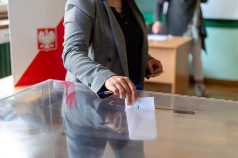 Osoba wrzuca złożona kartę do głosowania do przezroczystej urny wyborczej