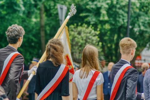 Czworo uczniów ubranych na galowo stoi trzymając sztandar szkoły podczas uroczystości szkolnej