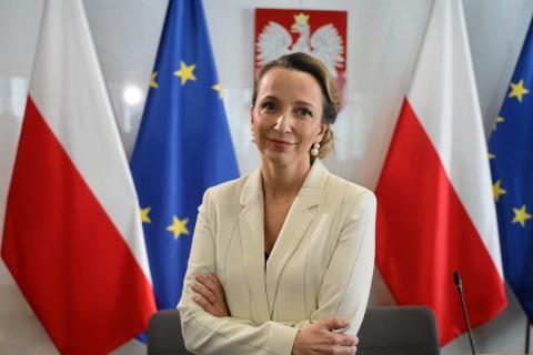 Zdjęcie portretowe kobiety na tle flag Polski i UE i polskiego godła