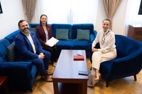 Trzy osoby siedzą na sofach przy stoliku kawowym i pozują do wspólnego zdjęcia