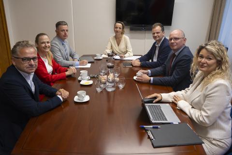 Siedem osób siedzi przy stole konferencyjnym i uśmiecha się pozując do zdjęcia
