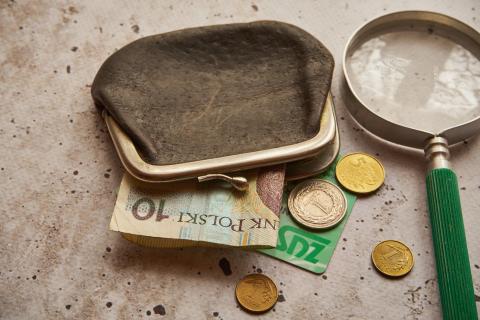portmonetka obok której leży banknot i bilon oraz lupa powiększająca
