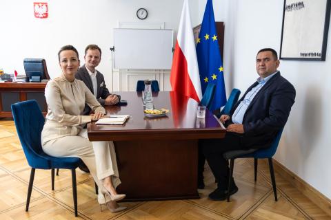 Trzy osoby siedzą przy stole i pozują do wspólnego zdjęcia