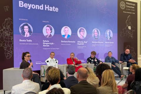 Siedem osób siedzi w fotelach na scenie podczas panelu dyskusyjnego