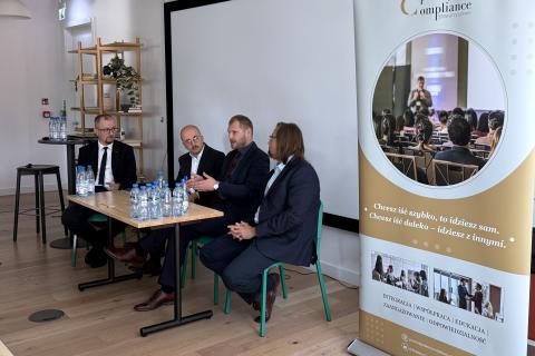 Cztery osoby siedzą przy stole na sali konferencyjnej i rozmawiają