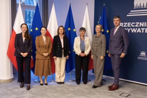 Sześć osób pozuje do wspólnego zdjęcia na tle flag Polski i UE