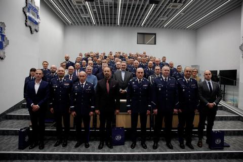 Kilkadziesiąt osób pozuje na stojąco do wspólnego zdjęcia na sali wykładowej