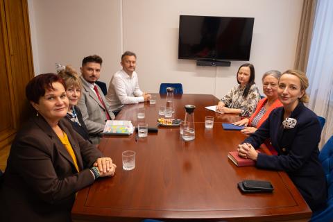 Siedem osób siedzi przy stole w salce konferencyjnej