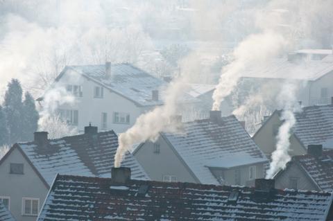 Dachy budynków jednorodzinnych z kominami, z których leci dym