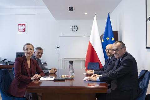 Cztery osoby pozują do zdjęcia siedząc przy stole w gabinecie Rzecznika. W tle flagi Polski i Unii Europejskiej