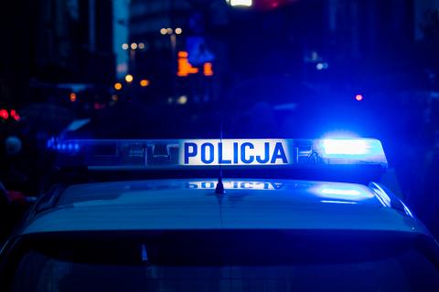 Błyskające błękitnym kolorem lampy na dachu radiowozu policyjnego. Na środku lampy jest napis "Policja"